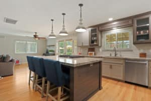 A remodeled kitchen featuring an island with blue bar chairs, modern cabinetry, and stylish light fixtures